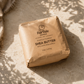 A 5 lb brown paper bag of FairTale Ghana Shea Butter, photographed from an overhead angle on a textured beige stone surface with dappled sunlight and shadows.